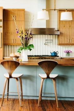 two wooden chairs sitting in front of a kitchen island with flowers on top of it