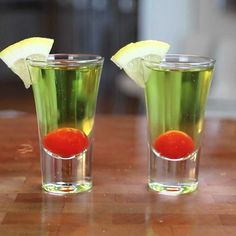 two shot glasses filled with liquid and lemon wedges on top of a wooden table