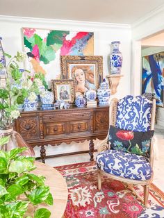 an ornately decorated living room with blue and white furniture, potted plants and paintings on the wall