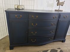 a large blue dresser with brass handles on it's doors and drawers, in front of a white wall