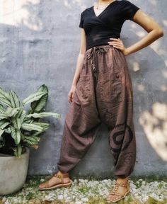 a woman leaning against a wall with her hands on her hips wearing brown pants and sandals