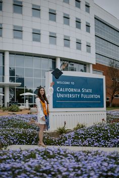 a woman standing in front of the california state university tillon sign with purple flowers around her