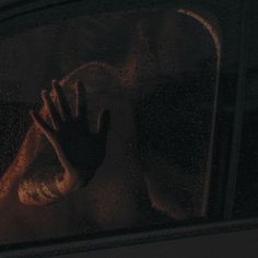 a person standing in front of a window covered in rain