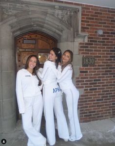 three women in white outfits are posing for a photo outside an old brick building with the door open