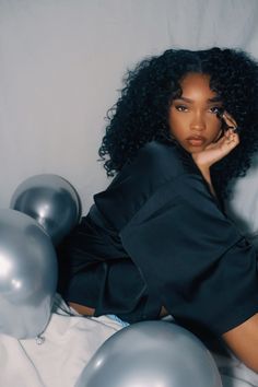 a woman laying on top of a bed next to balloons and silver balls in front of her