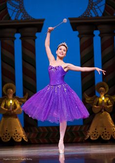 a young ballerina is dressed in purple tutu and has her arms up as she performs