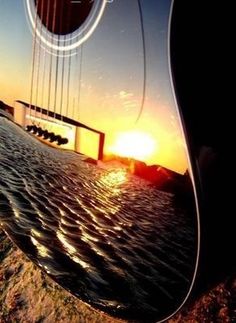 the sun is setting behind a bridge over water with waves in front of it and an acoustic guitar hanging from its neck