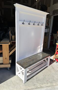 a wooden bench sitting in front of a white shed with hooks on it's doors