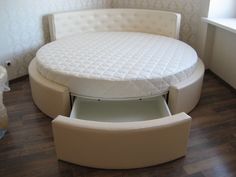 a round bed sitting on top of a hard wood floor next to a white couch