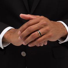 a man in a black suit and white shirt holds his hands together while wearing two wedding bands