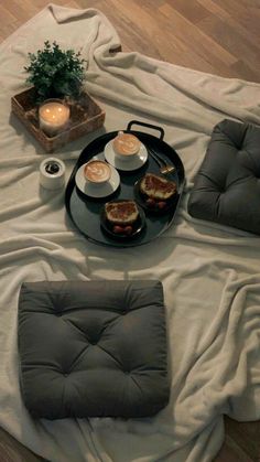 a table topped with plates and cups filled with food next to candlelight candles on top of a white blanket