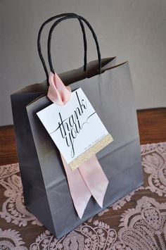 a black shopping bag with a pink ribbon tied around it and a thank you sign on the front