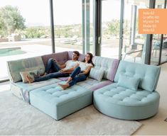 a man and woman sitting on a couch in front of a large window with an orange sign