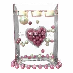 a glass vase filled with pink and white pearls next to two votive candles in the shape of a heart