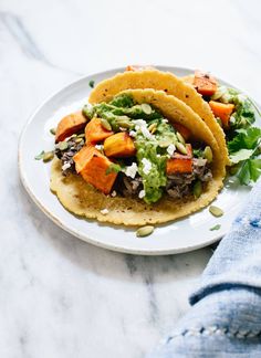 three tacos on a white plate with guacamole and other toppings