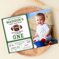 a football ticket for a baby's first year birthday is displayed on a wooden plate