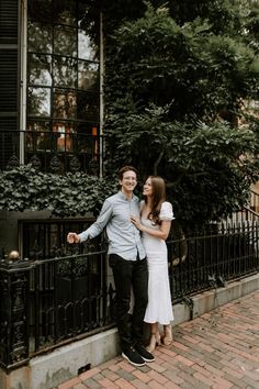 a man and woman standing next to each other in front of a black iron fence