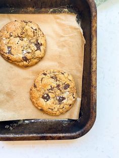 two chocolate chip cookies sitting on top of a baking sheet in an oven pan with parchment paper