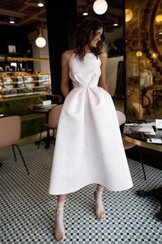 a woman in a white dress standing next to a dining room table with chairs and tables