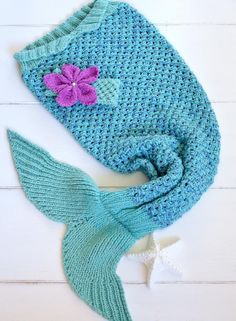 a crocheted mermaid tail with a pink flower on it and a blue knitted hat