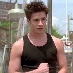 a young man in a black tank top is looking at the camera while standing outside