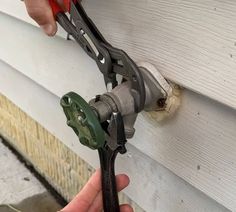 a person is holding some pliers in front of a white house that has siding on it