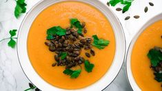 two white bowls filled with carrot soup and garnished with herbs