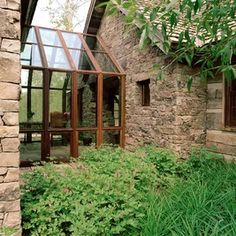 an old stone house is surrounded by greenery and flowers in the foreground, with large windows to let in light