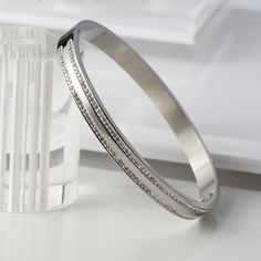 Gold and silver tone bangle with two rows of CZ stones throughout. Bangle features a snap closure and a high shine finish. Made of premium grade stainless steel, hypoallergenic and tarnish resistant. It is easy to wear and can be worn by itself or added to a stacking bracelet collection. It is the perfect gift for any woman. - Stones Material: Cubic Zirconia.- Stones Shape: Round.- Metal: Stainless Steel.- Plating: 18k Gold plated or Rhodium plated.- Interior Diameter: 58.5 mm.- Width: Aprox. 6 Modern Silver Cuff Bracelet With Diamond Accents, Classic Silver Bangle With Channel Set, Classic Silver Channel Set Bangle, Silver Channel Set Bangle For Anniversary, Silver Stainless Steel Bangle For Anniversary, Silver Stainless Steel Anniversary Bangle, Silver Stainless Steel Bracelets With Diamond Accents, Silver Stainless Steel Crystal Bracelet, Silver Stainless Steel Bangle Crystal Bracelet