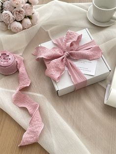 a pink ribbon tied to a white box on a table next to flowers and a cup