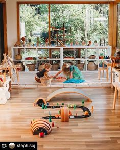 two children playing with wooden toys in a room filled with wood flooring and windows