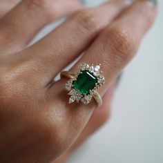 a close up of a person's hand wearing a ring with an emerald and diamond center