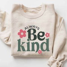 a sweater with the words always be kind printed on it and flowers in pink, green, and black