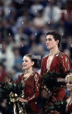 two young people in red and gold costumes, one is holding a wreath while the other holds