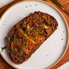 a white plate topped with meat covered in sauce and garnished with green herbs