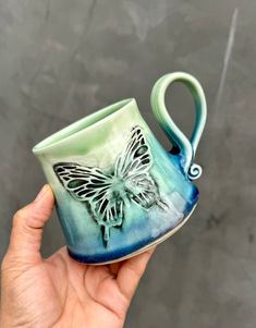 a hand holding a blue and green cup with a butterfly on it