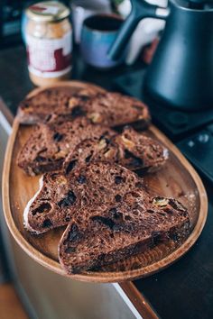 chocolate cake on a wooden platter sitting on a counter next to a coffee pot