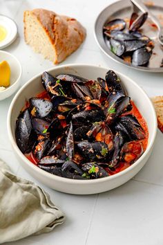 there is a bowl of mussels on the table with bread and other dishes