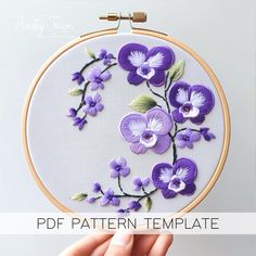 a hand is holding up a purple flower embroidery pattern