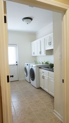 an open door leading to a washer and dryer in a room with white cabinets