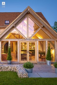 a large wooden house with glass windows and plants in the front yard at night time