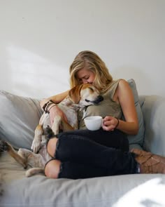 a woman sitting on a couch with her dog and drinking from a coffee cup while holding a mug