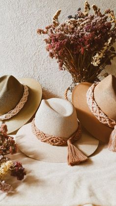 three hats sitting on top of a bed next to dried flowers