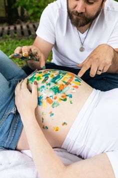 a man is painting the belly of a pregnant woman with colorful paint on her stomach