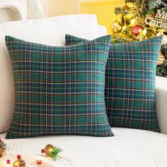 two green plaid pillows sitting on top of a white couch next to a christmas tree