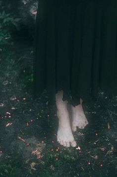 a woman standing in the grass with her bare feet propped up on top of her skirt