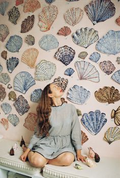 a woman sitting on top of a white table in front of a wall covered with paper fans