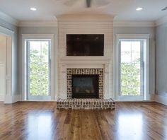 a living room with hard wood floors and a fireplace in the center, two windows on both sides