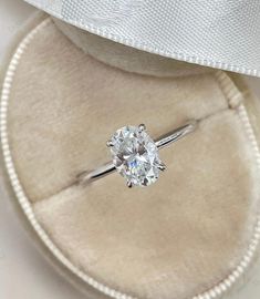 an engagement ring in a velvet box with a white ribbon around the band and a diamond center stone