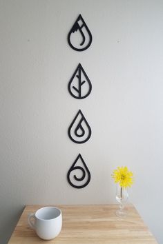 three metal water drop wall art pieces on a table next to a vase with a yellow flower in it